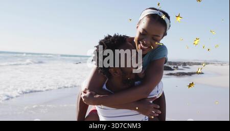 Lächelnder Mann in gestreiftem Hemd Huckepack Frau mit Haarreif am Strand, mit goldenen Sternen-Überzügen Stockfoto