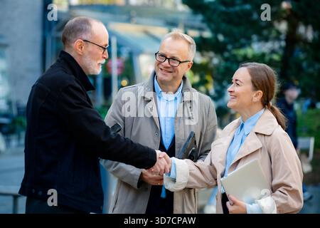 Glückliche Geschäftsleute, die in der City Street im Freien mit dem Handshake arbeiten, Partnerschaften feiern oder erfolgreiche Bewerbungsgespräche führen Stockfoto