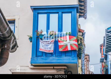 Blauer Balkon mit Ikurrnia-Flagge und Social Protest Banner, Straßenblick auf das traditionelle Gebäude im Baskenland, Spanien Stockfoto