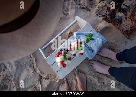 Picknick am Strand, Dessertszene mit erfrischendem Fruchtsorbet, Himbeeren, Minzblättern und barfuß-Entspannung im Sommer auf Sand von oben. H. Wird erstellt Stockfoto