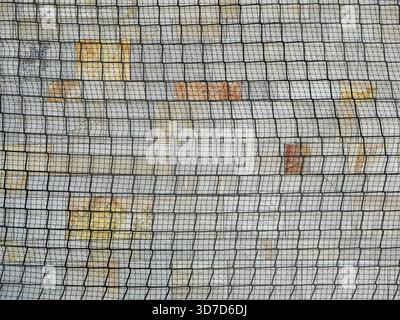 Die schützende und verdeckende Funktion des Netzgewebes an der beschädigten Fassade erzeugt durch seine Überlappung eine visuelle Spannung und eine grafische Qualität Stockfoto