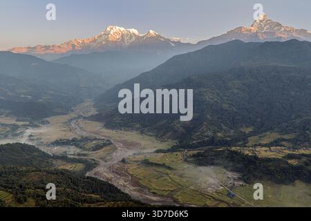 Aus der Vogelperspektive auf die majestätische, schneebedeckte Annapurna-Bergkette, die den Himmel über üppigen Tälern und gewundenen Flüssen durchsticht, Astam, Provinz Gandaki, Nepal. Stockfoto