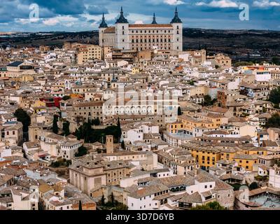 Blick aus der Vogelperspektive auf die Alcázar de Toledo, die stolz über der dicht gepackten Stadt steht, deren Steinmauern einen starken Kontrast zu den Terrakottadächern darunter bilden Stockfoto
