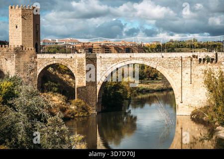 Blick aus der Vogelperspektive auf die alte Steinbrücke von San Martín, die sich anmutig über den Tejo erhebt, deren Spiegelbild im Wasser schimmert, Toledo, Spanien. Stockfoto