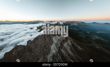 Aus der Vogelperspektive sehen Sie zerklüftete Gipfel, die durch ein Wolkenmeer durchdringen, im Kontrast zu den grünen Tälern darunter, Karersee, Trentino-Südtirol, Italien. Stockfoto