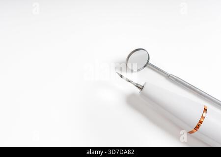 Ein Zahnspiegel und ein Handstückwerkzeug, das ordentlich auf weißem Hintergrund platziert ist und professionelle zahnmedizinische Geräte zeigt. Stockfoto