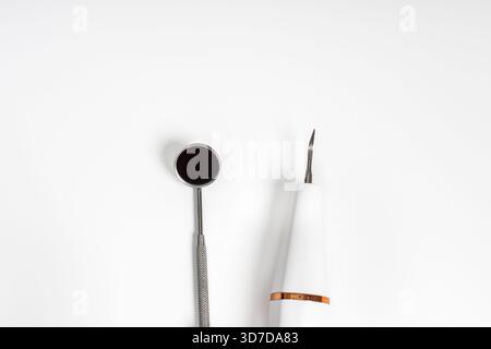 Ein Zahnspiegel und ein Handstückwerkzeug, das ordentlich auf weißem Hintergrund platziert ist und professionelle zahnmedizinische Geräte zeigt. Stockfoto