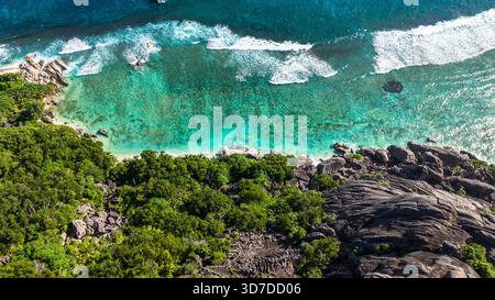 Blick von oben auf felsige Formationen am Ufer mit klarem türkisfarbenem Wasser. La Digue, Seychellen. Stockfoto