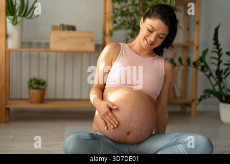Eine sportlich schwangere Frau in aktiver Kleidung macht Übungen auf Yogamatten. Stockfoto