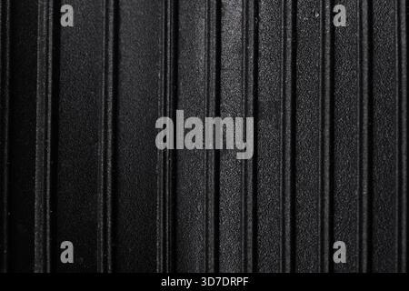 Nahaufnahme der schwarzen Oberfläche mit gleichmäßig abgesetzten vertikalen Graten, die einen modernen, minimalistischen, strukturierten Hintergrund für vielseitiges kommerzielles Design schaffen Stockfoto