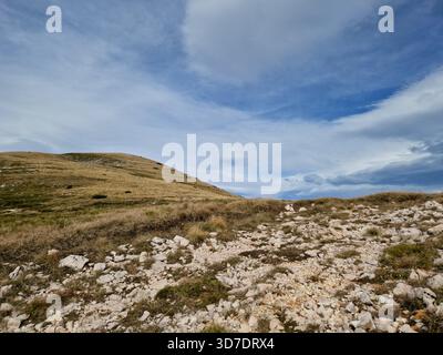 Eine ruhige Sommerlandschaft an den felsigen Hängen des Cincar Mountain in Bosnien und Herzegowina mit goldenen Grasland und verstreuten Steinen. Stockfoto