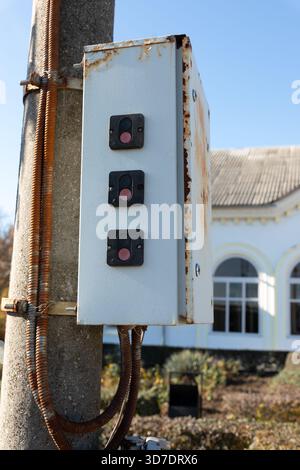 Nahaufnahme eines Außenbedienfelds aus Metall mit drei Knöpfen an einem Stab, das Rost und Verschleiß vor einem verschwommenen Gebäudeschutz zeigt. Stockfoto