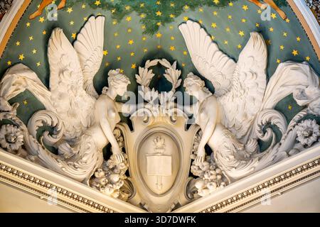 Library of Congress Jefferson Building Great Hall Angels Washington DC / WASHINGTON DC – geflügelte allegorische Figuren, allgemein als Engel bezeichnet, zieren die kunstvolle Decke der Great Hall im Library of Congress Thomas Jefferson Building. Diese detaillierten weißen Skulpturen stehen vor einem sternenklaren, dunkelgrünen Hintergrund und tragen ein zentrales Emblem mit offenem Buch und Taschenlampe. Sie sind integraler Bestandteil des aufwändigen architektonischen und künstlerischen Beaux-Arts-Entwurfs des Gebäudes, das 1897 fertiggestellt wurde. Das Thomas Jefferson Building ist das älteste Gebäude der Library of Congress, bekannt für seine reiche Symbolik und dez Stockfoto