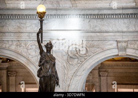 WASHINGTON DC – Eine bronzene Fackelträgerskulptur von Philip Martiny befindet sich am Fuße der großen Treppe im Great Hall of the Library of Congress Thomas Jefferson Building. Diese Figur, die mit klassischen Vorhängen verkleidet ist und eine Fackel des Wissens hält, ist Teil des ausgeklügelten skulpturalen Programms, das das Innere des Gebäudes schmückt. Martys umfangreiches Werk umfasst auch Putten aus weißem Marmor, die die Treppengeländer schmücken und verschiedene Berufe und Verfolgungen des modernen Lebens darstellen, wie z. B. einen Musiker, Arzt und Astronomen. Das 1897 fertiggestellte Thomas Jefferson Building ist das alte Gebäude Stockfoto