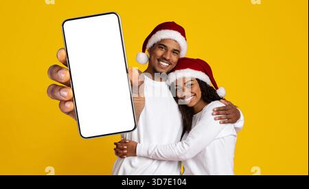 Ein Paar lächelt und zeigt ein leeres Smartphone während der Weihnachtszeit Stockfoto