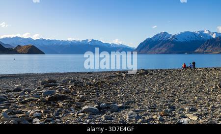 Ein felsiger Strand am Ufer des Lake Hawea auf der Südinsel Neuseelands. Im Hintergrund liegen die schneebedeckten Berge der Südalpen Stockfoto