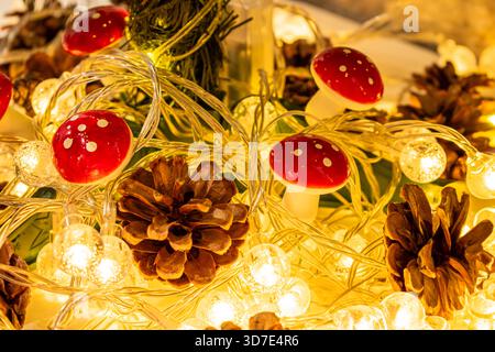 Weihnachtsdekoration und -Einrichtung. Eine glühende Girlande mit warmem Licht, Tannenzapfen und pilzförmigen Ornamenten. Stockfoto