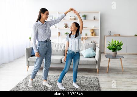 Fröhliche Mutter und Tochter tanzen zusammen im Wohnzimmer und genießen die Familienzeit Stockfoto