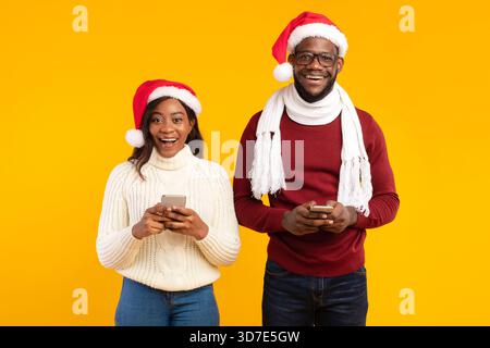 Paare in Santa Hats mit Smartphones und lächeln in einem Studio an Weihnachten Stockfoto