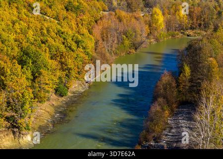 Aus der Vogelperspektive des Venezikos River, der sich durch den lebhaften Herbstwald in Westmakedonien, Griechenland, mit einer parallelen Straße, die in das natürliche Land mündet Stockfoto