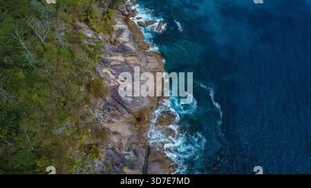 Zerklüftete tropische Küste mit Granitfelsen, stürzenden Wellen und tiefblauem Wasser Stockfoto