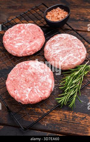 Gefrorene Fleischpasteten, bereit zum Grillen, Forcemeat von Schwein und Rindfleisch für Burger. Hölzerner Hintergrund. Draufsicht. Stockfoto