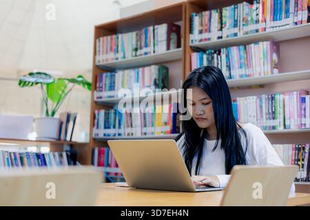 Asiatische Studentin, die Laptop in einer modernen Bibliothek benutzt, konzentriert sich auf das Lernen und Online-Lernen. Bildung, Forschung, Technologie und akademischer Lebensstil Stockfoto