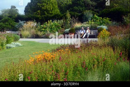 Ältere Ehepaare sitzen auf einer Holzbank und bewundern die Grenzen im RHS Garden Harlow Carr, Harrogate, Yorkshire, England, Großbritannien Stockfoto