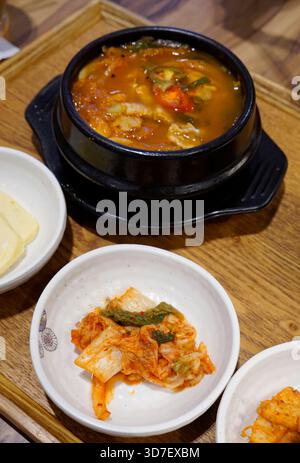 Koreanische Tofu-Suppe Kimchi jjigae in einer beheizten Steinschale mit Beilagen Stockfoto