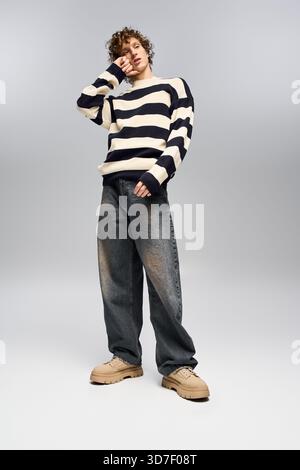 Ein stilvoller junger Mann posiert selbstbewusst in einem gestreiften Pullover und einer Baggy-Jeans und strahlt Charme aus. Stockfoto
