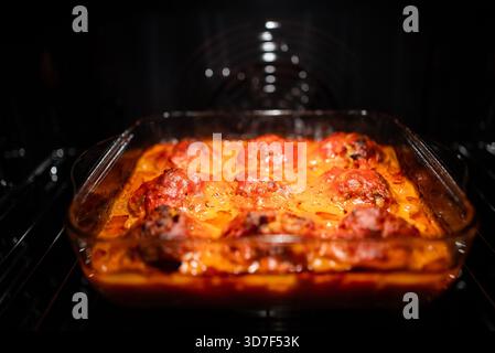 Hausgemachte Fleischbällchen, die in einer lebendigen Tomatensauce in einem klaren Glas-Auflauf köcheln, in einem warmen Ofen braten und eine köstliche kulinarische Kreation zum Abendessen präsentieren Stockfoto
