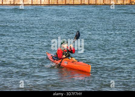 Älterer oder älterer Mann, der auf einem ruhigen Meer mit Winterkajakkleidung paddelt. Stockfoto