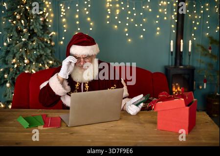 Der Weihnachtsmann liest Kinderbriefe auf dem Computer und bestellt online Stockfoto