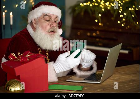 Der Weihnachtsmann liest Kinderbriefe auf dem Computer und bestellt online Stockfoto