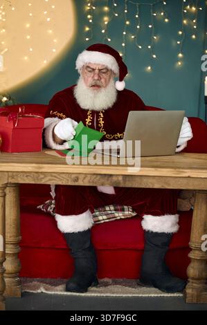 Der Weihnachtsmann liest Kinderbriefe auf dem Computer und bestellt online Stockfoto