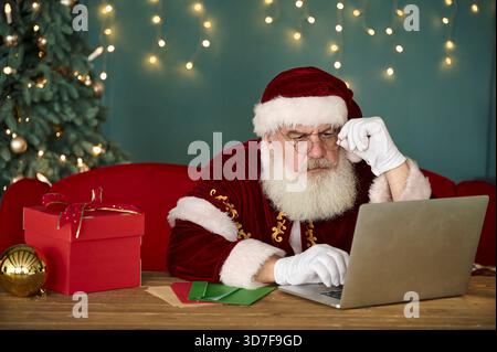 Der Weihnachtsmann liest Kinderbriefe auf dem Computer und bestellt online Stockfoto