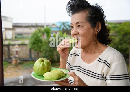 Eine alte Frau isst Guavas vor einem Gartenhintergrund. Stockfoto