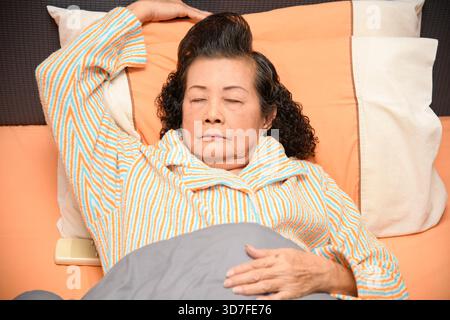 Eine alte Frau schläft auf dem Bett in ihrem Schlafzimmer. Stockfoto