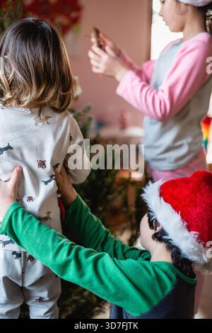 Drei Mädchen im Schlafanzug schmücken den weihnachtsbaum zu Hause Stockfoto