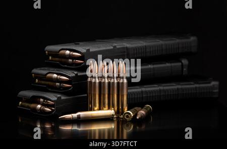 Gewehrmunition und geladene schwarze Polymermagazine werden vor einem dunklen, reflektierenden Hintergrund angezeigt. Stockfoto