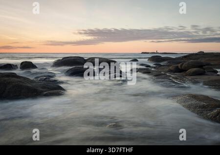 Sanfte Wellen ziehen bei Sonnenuntergang an uruguays ruhiger Küste über Felsen Stockfoto