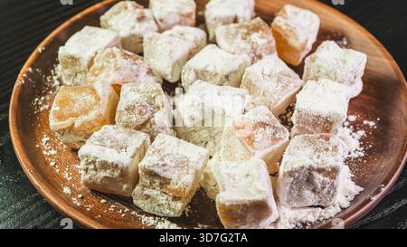 Verschiedene türkische Köstlichkeiten auf einem rustikalen Holzteller. Farbenfrohe, mit Zucker verstaubte Süßigkeiten mit Aromen wie Rose, Zitrone und Pistazien. Traditionelle Mittlere Eas Stockfoto