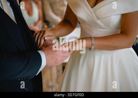 Ein Mann und eine Frau heiraten. Der Mann trägt einen Anzug und die Frau trägt ein weißes Kleid. Sie tragen beide Eheringe Stockfoto