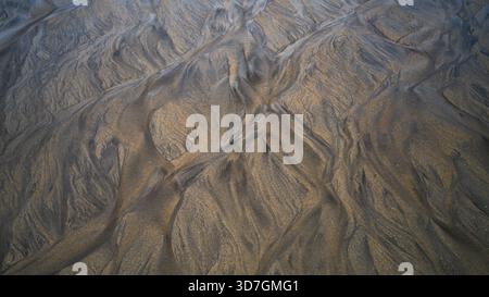 Abstrakte Sandmuster, die von Gezeitenwasser an einem Küstenstrand geformt werden. Stockfoto