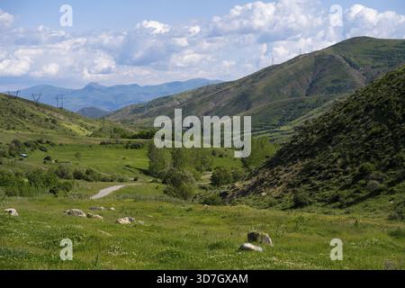 Bergiges Tal mit grüner Wiese unter blauem Himmel mit Wolken und Stromleitungen, Landschaft von Süden in Richtung Vardenyats Pass oder Selim Pass, Vayots Stockfoto