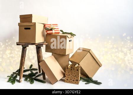 Pappkartons und Pakete in verschiedenen Größen, alter Hocker und Kiefernzweige vor hellem Hintergrund mit Bokeh und Glitzern, Weihnachtsgeschenke, Packagi Stockfoto