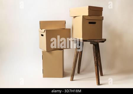 Pappkartons und Pakete auf einem alten Hocker und auf dem Boden in verschiedenen Größen, vor hellbeigem Hintergrund, Konzept für Weihnachtsgeschenke, Packagi Stockfoto