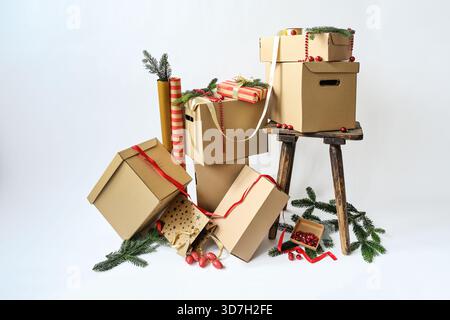 Kartonschachteln in verschiedenen Größen, Geschenkpapier, Band und Tannenzweige vor hellem Hintergrund, Konzept für Weihnachtsgeschenke, Verpackung und Tische Stockfoto