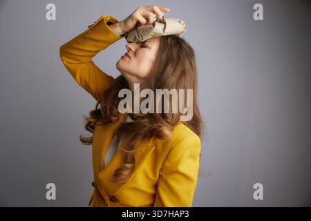 Eine Geschäftsfrau mit geschlossenen Augen und nach hinten geneigtem Kopf legt sanft ein Eispack auf ihre Stirn und sucht Linderung von Unannehmlichkeiten oder dem Druck von h Stockfoto