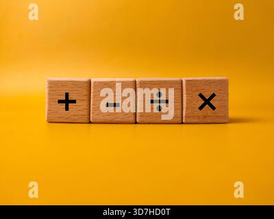 Das Bild zeigt vier Holzblöcke mit grundlegenden mathematischen Betriebssymbolen auf gelbem Hintergrund. Stockfoto